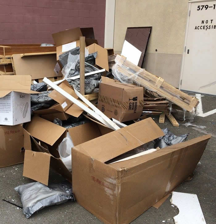 Piles of discarded cardboard boxes and various debris stacked messily in an outdoor area next to a building exit door.