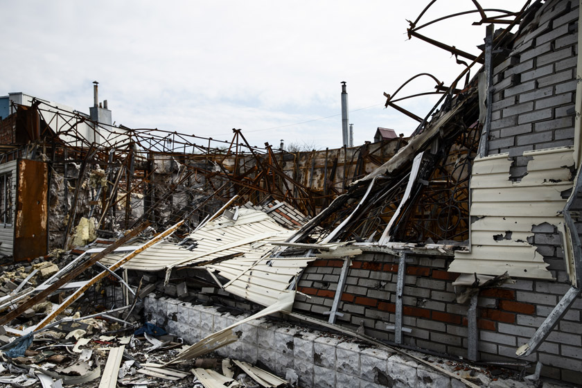 A collapsed building with exposed twisted metal and debris scattered on the ground under a cloudy sky.