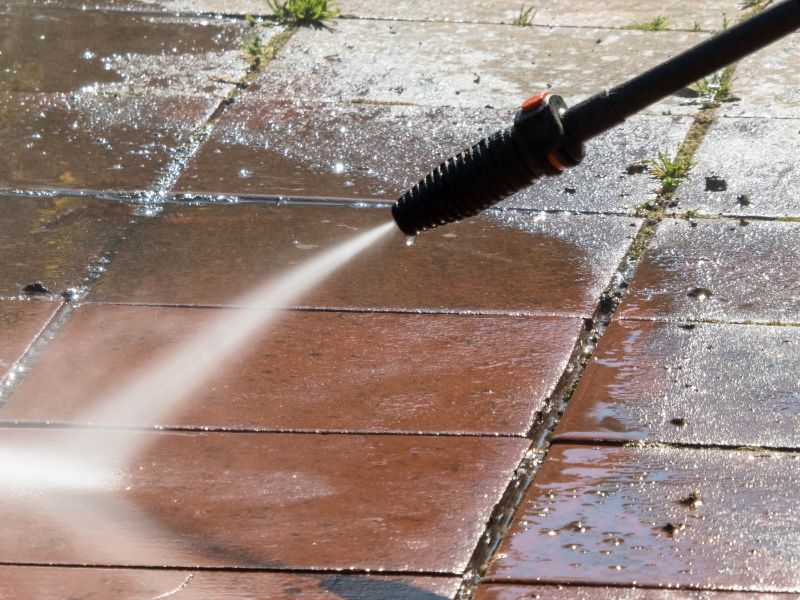 A pressure washer sprays water on a red tiled surface, cleaning dirt and grime off the tiles.